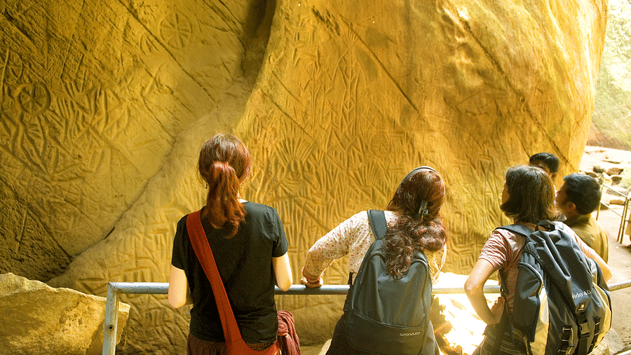 A back view of people holding grills and looking at a huge rock | Vythiri Resort, Wayanad